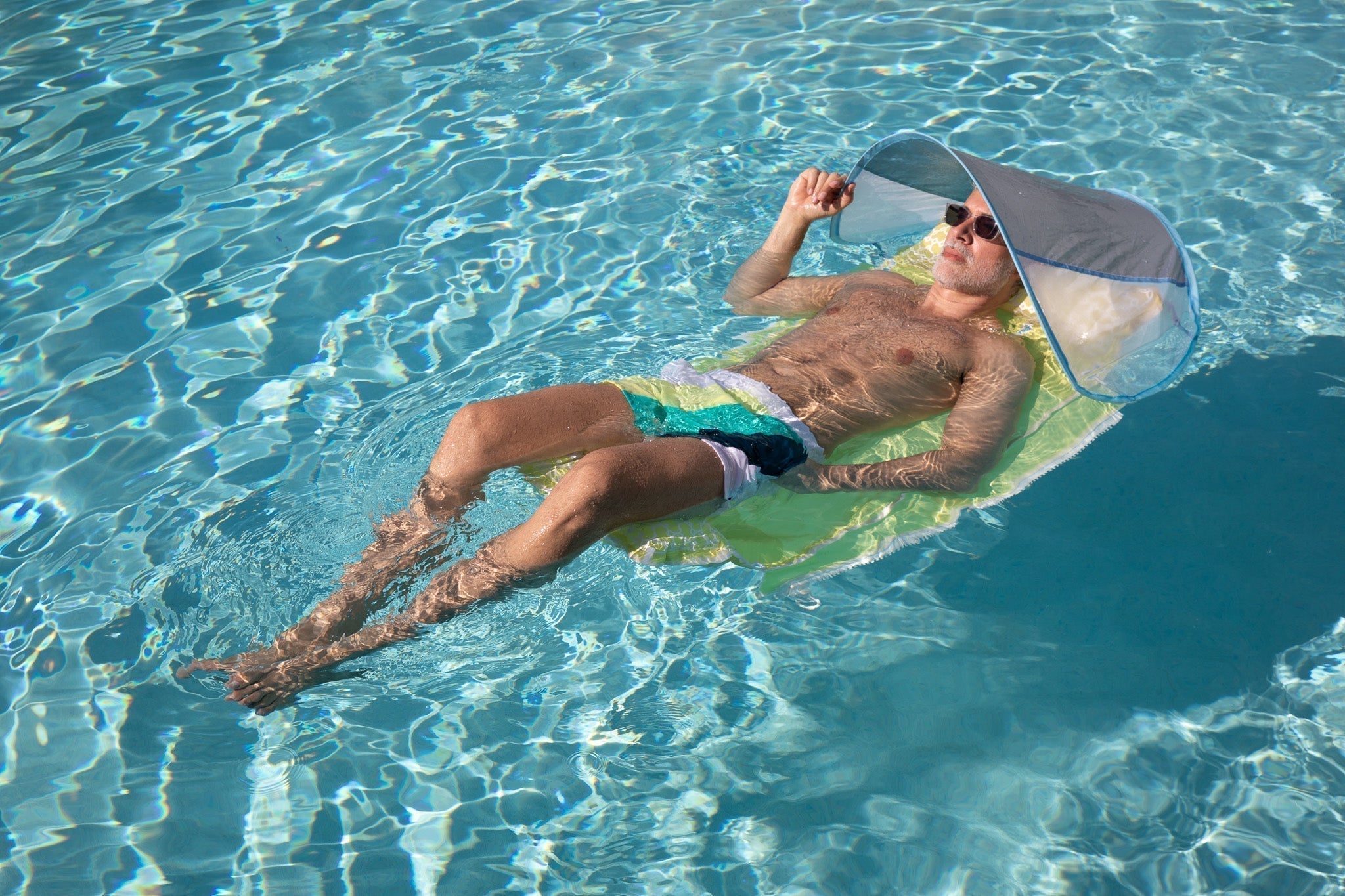 man floating on water with Sand2Sea inflatable beach bag and attached sunshade, enjoying the shade in a sunny pool